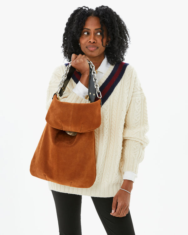 Mecca wearinga cream sweater and holding two chestnut suede bags