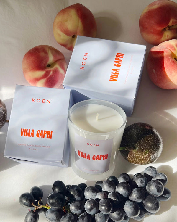 Roen Candle in the scent Villa Capri next to the candle box and some fruit