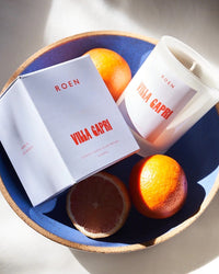 Roen Candle in the scent Villa Capri with its box on a bowl of fruit