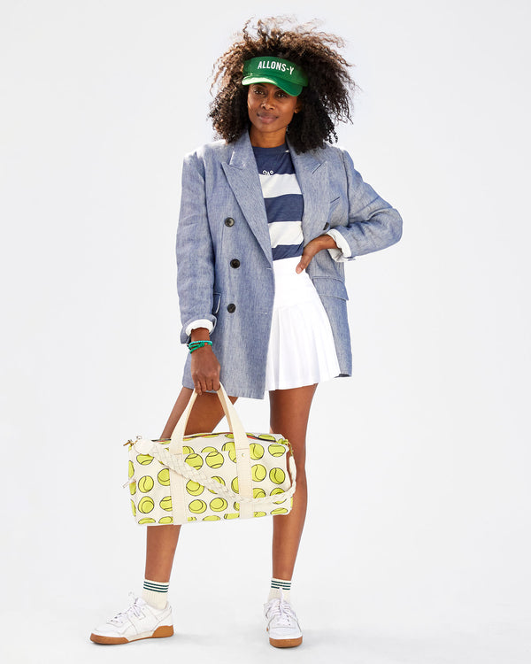 Mecca wearing a striped tshirt, a white tennis skirt, a blazer, the allons-y visor. she's carrying the Natural w/ Tennis Balls Duffle with the cream braided shoulder strap