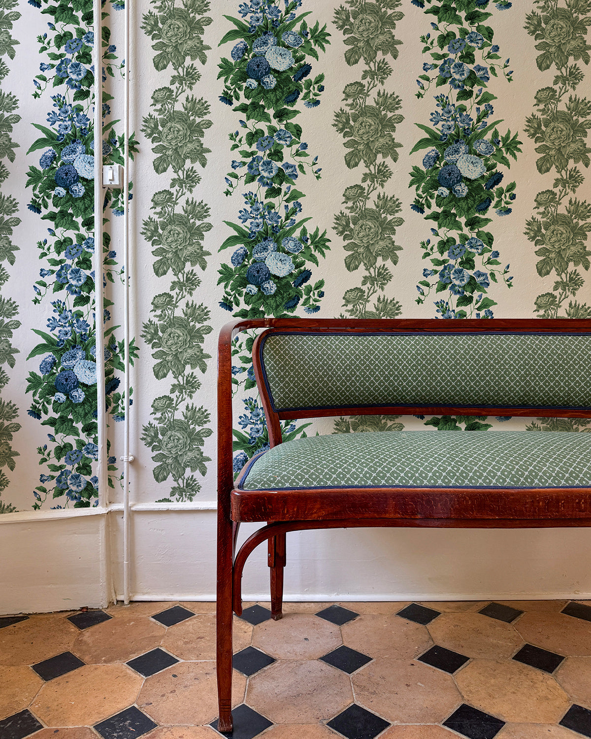 Room with tiled floor, a green upholstered chair, and the 'La Garland' in Blue Olive wallpaper. 