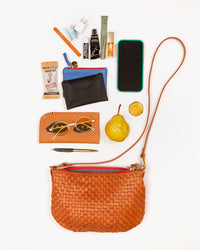 Natural Woven Petit Moyen with an iPhone, a card envelope, a coin clutch, a glasses sleeve, a pear, a small snack, a phone charger base and assorted other items