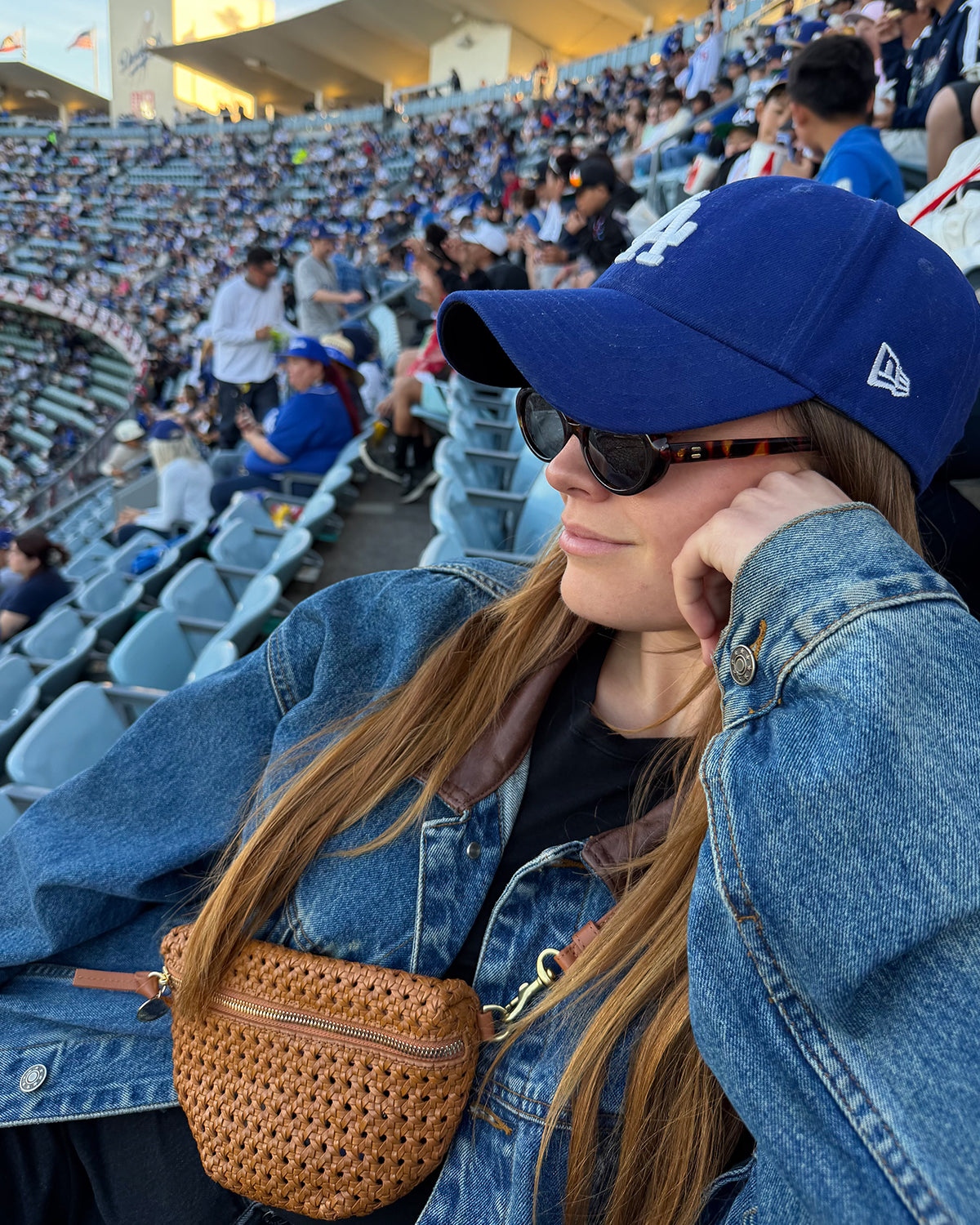 Woman at a Los Angeles Dodgers game wearing a denim jacket with the Tan Rattan Petite Fanny over the jacket and across her chest.