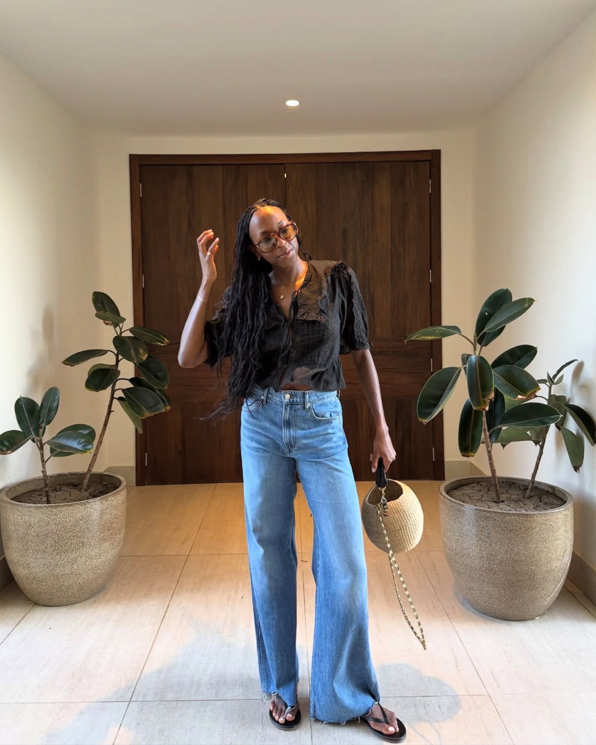Woman wearing blue jeans with a black blouse and carrying the Pot de Miel with a Chain Strap attached to it. 