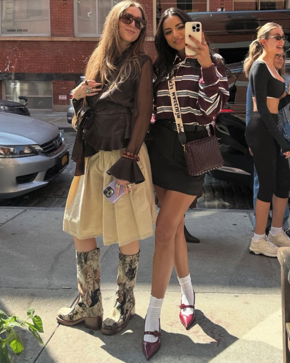 Two women taking a picture together. One of the women is carrying a Midi Sac with the Masculin Feminin Strap. 