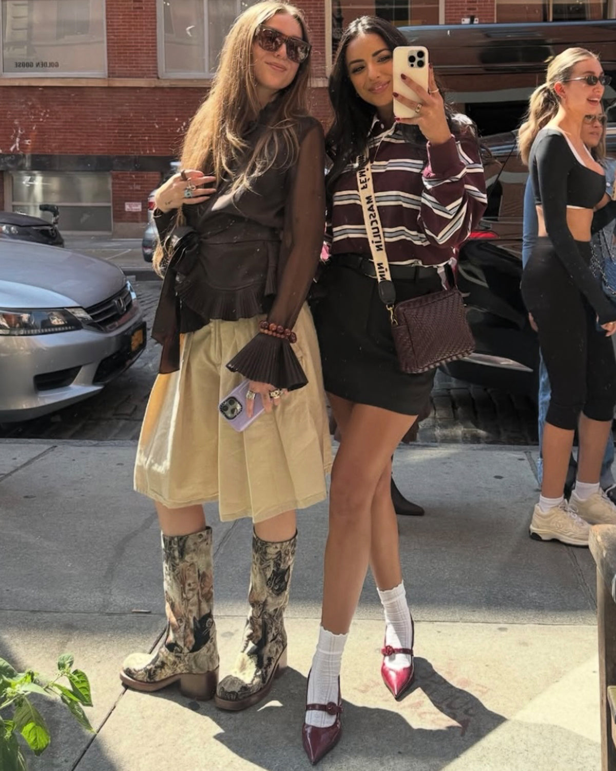 Two women taking a picture together. One of the women is carrying a Midi Sac with the Masculin Feminin Strap. 