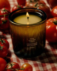 Flamingo Estate Roma Heirloom Tomato Candle sits among plump tomatoes on a red checkered tablecloth