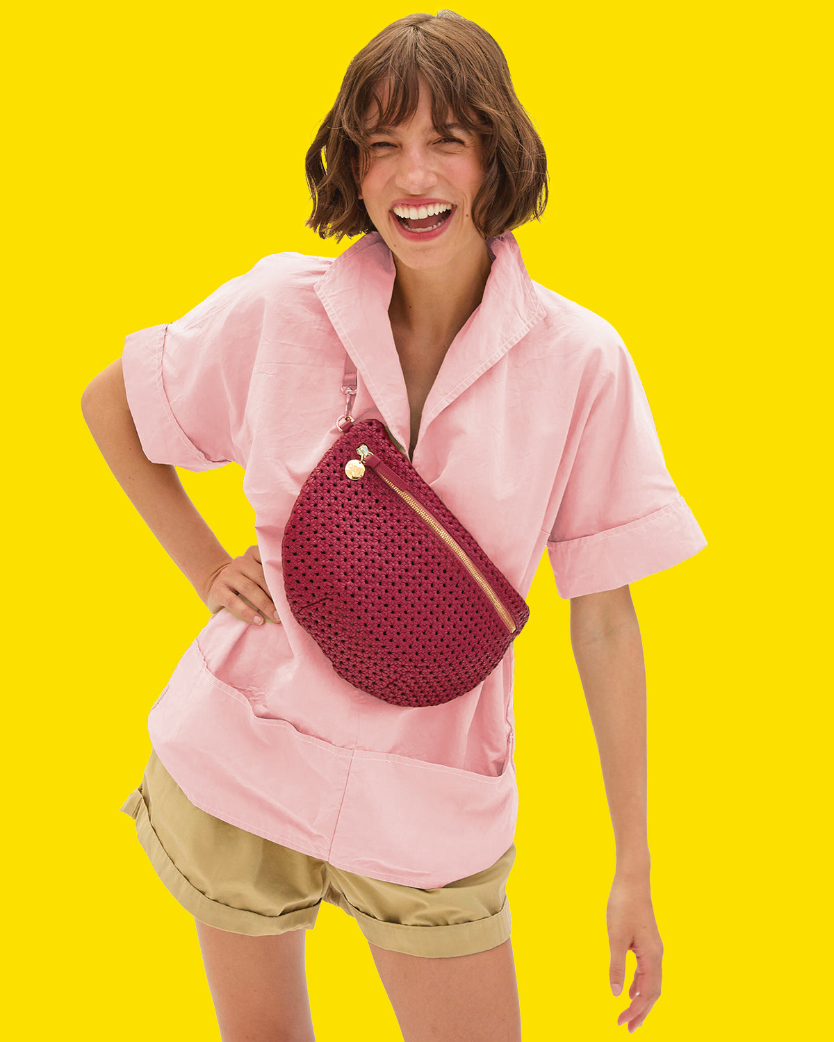 Model wearing a pink shirt and beige shorts with the Plummy Rattan Grande Fanny over her chest.