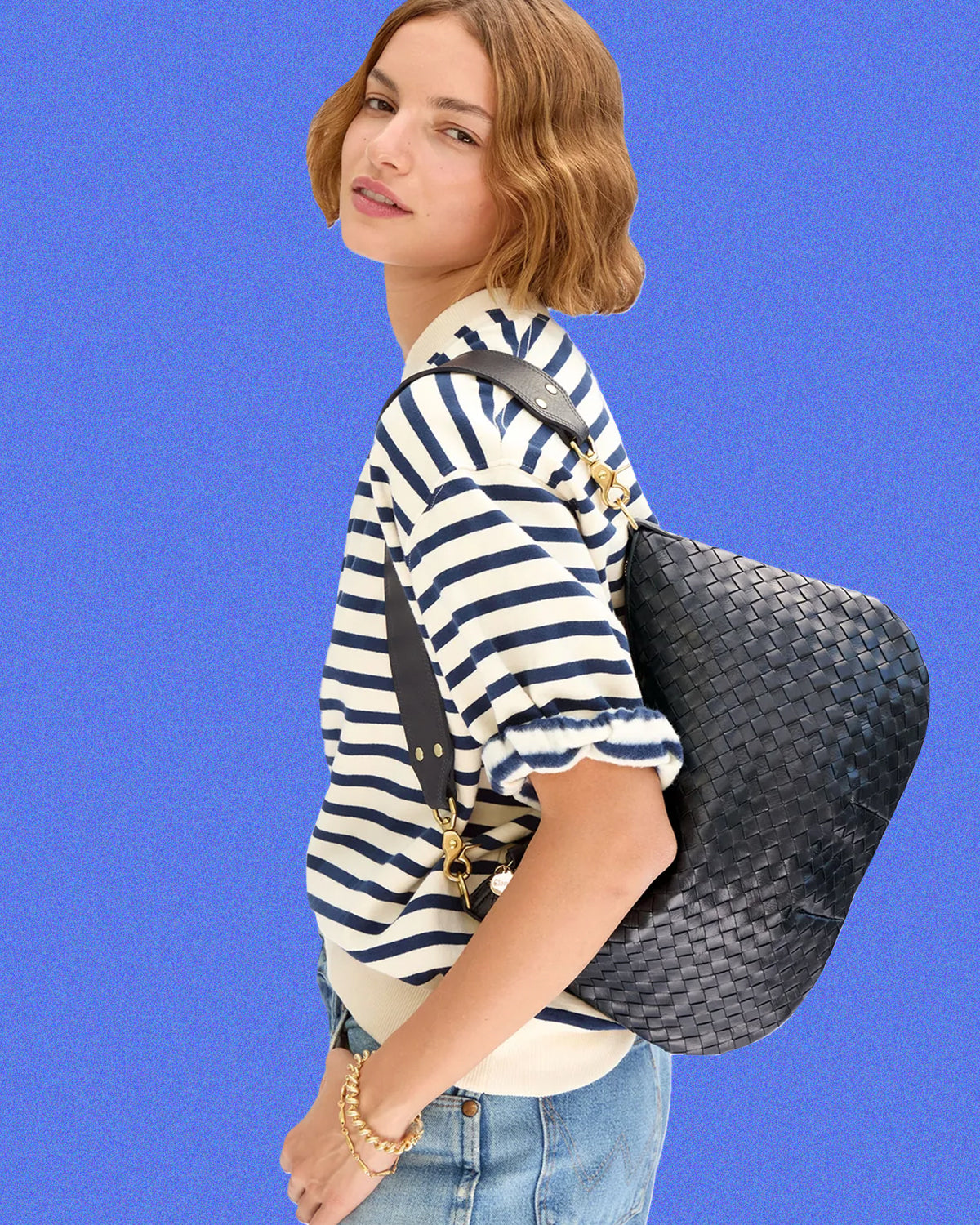 Model wearing the Cream/Navy Stripe Short Sleeve Oversized Sweatshirt with jeans and carrying the Twilight Navy Diagonal Woven Moyen Messenger over her shoulder. 