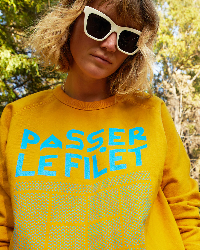Lou wearing the Marigold Passer Le FiLet Sweatshirt and our new Heather Sunglasses. Lou is standing in front of a beautiful background of green trees outside.