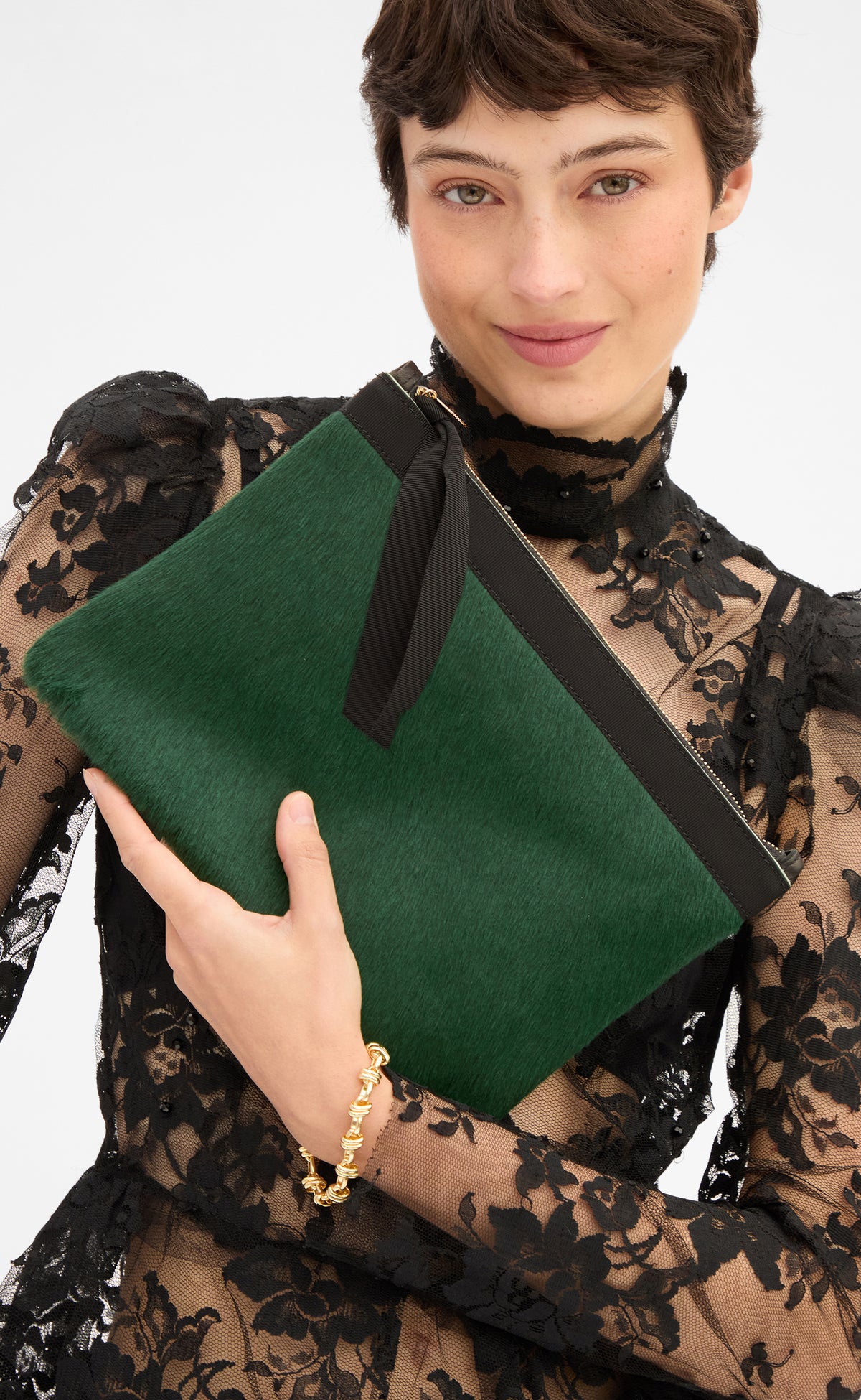 Model wearing a sheer black lace top and holding the Bottle Green Hair On Flat Clutch w/ Tabs. 