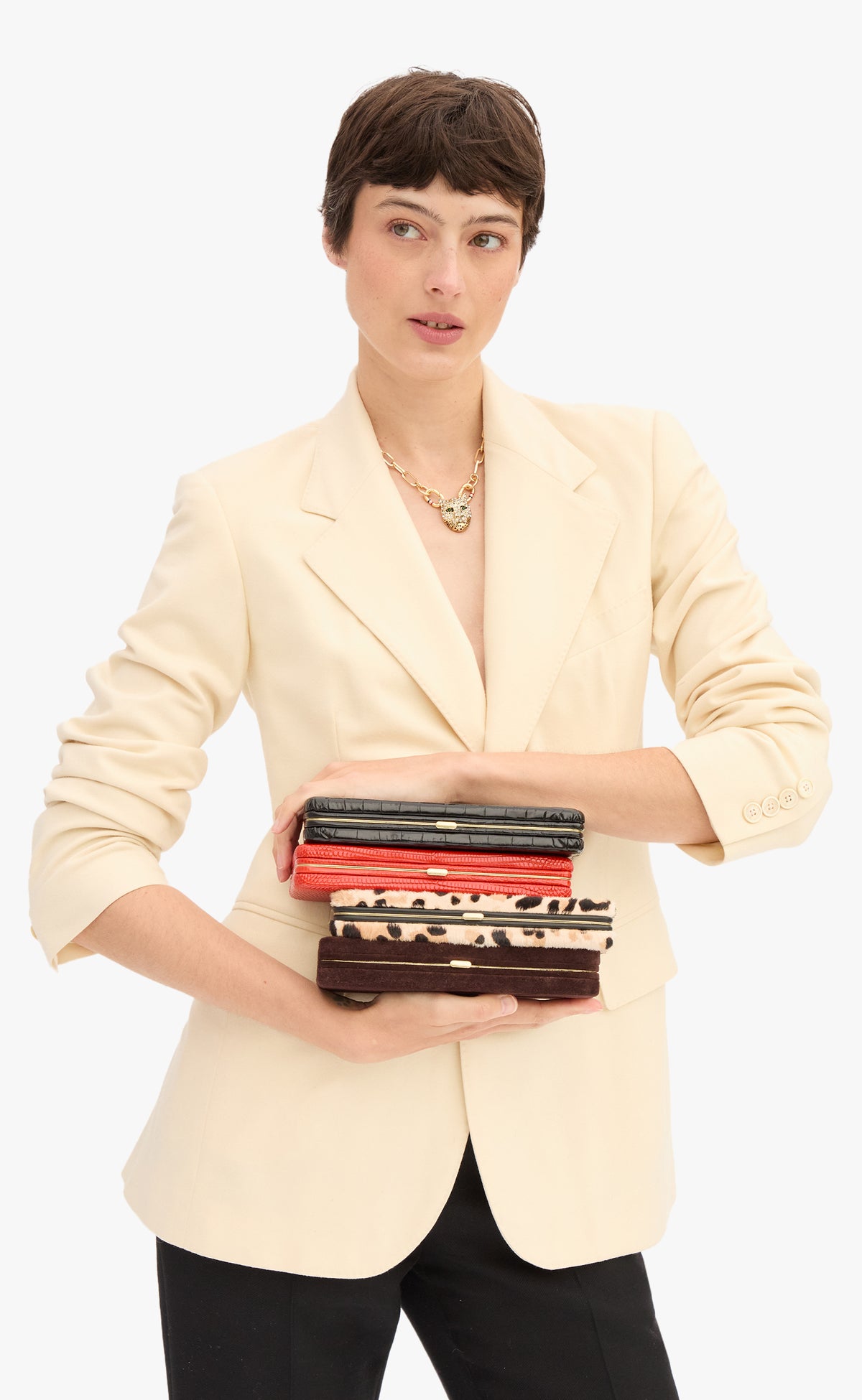 Model wearing a cream blazer with black pants and holding a stack of Le Tabac.