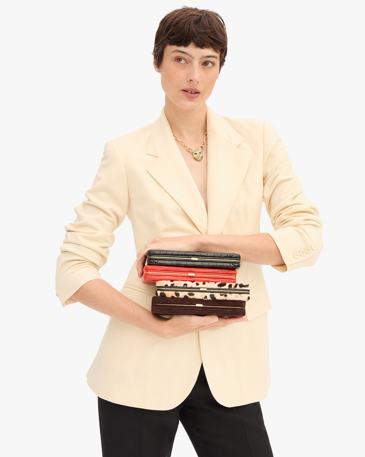 Model wearing a cream blazer with black pants and holding a stack of Le Tabac.