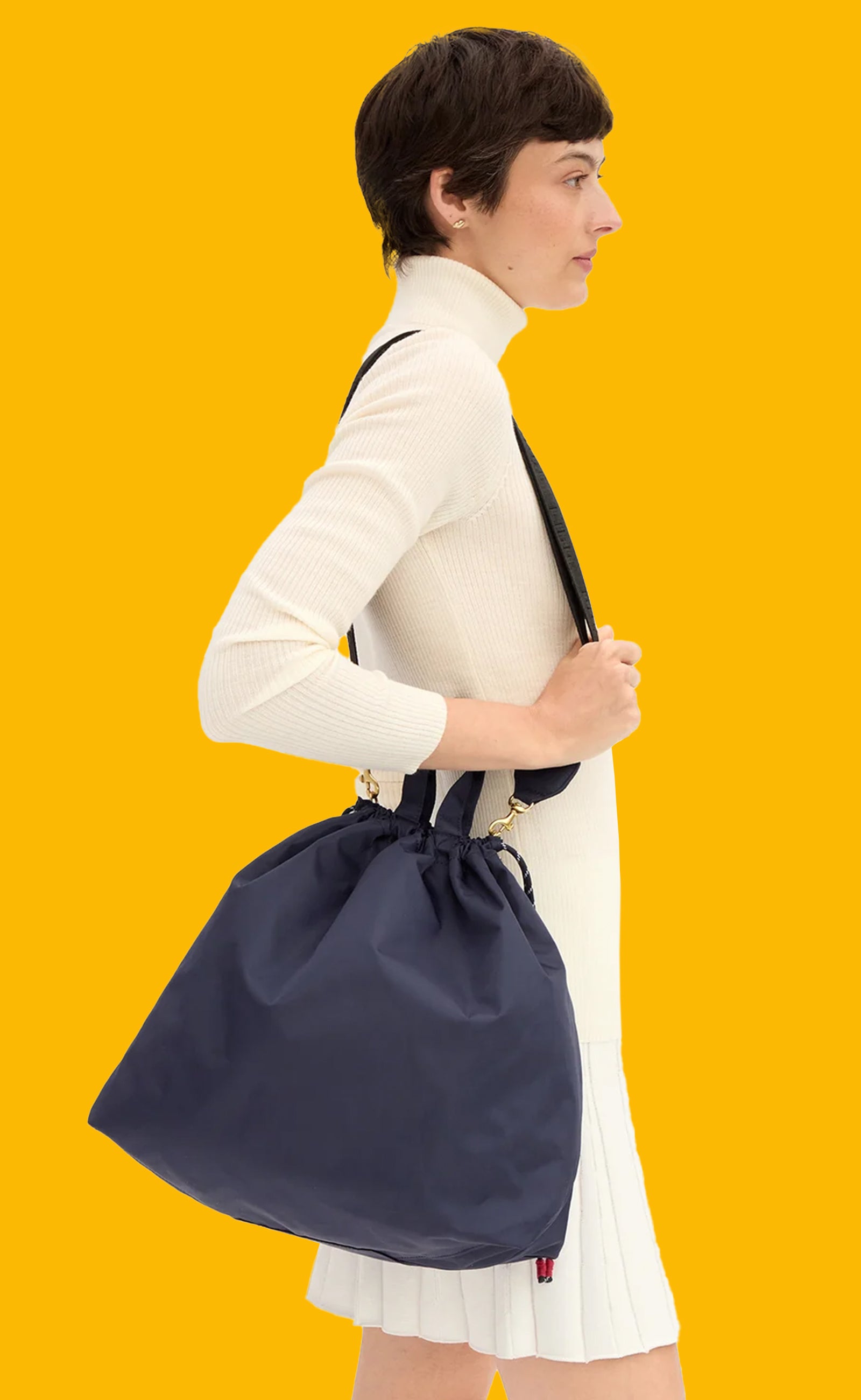 Model wearing a monochromatic cream outfit and carrying the Navy Sac Tout with the adjustable strap over her shoulder. 