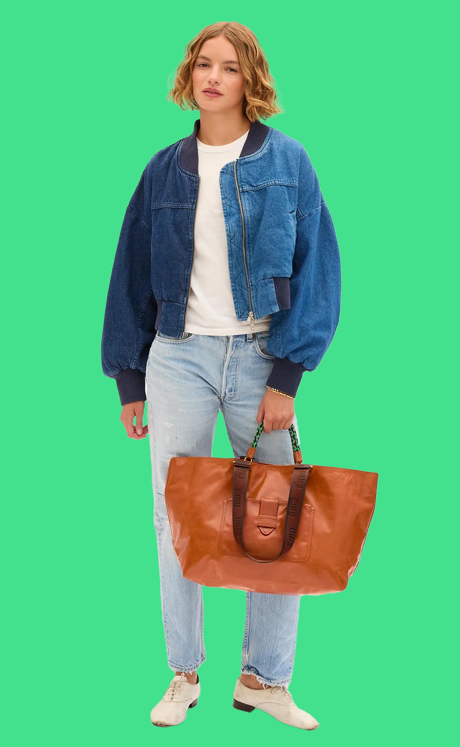 Model wearing jeans, a white t-shirt, and jean bomber jacket carrying the Camel Grande Bateau Tote by the top handle. 