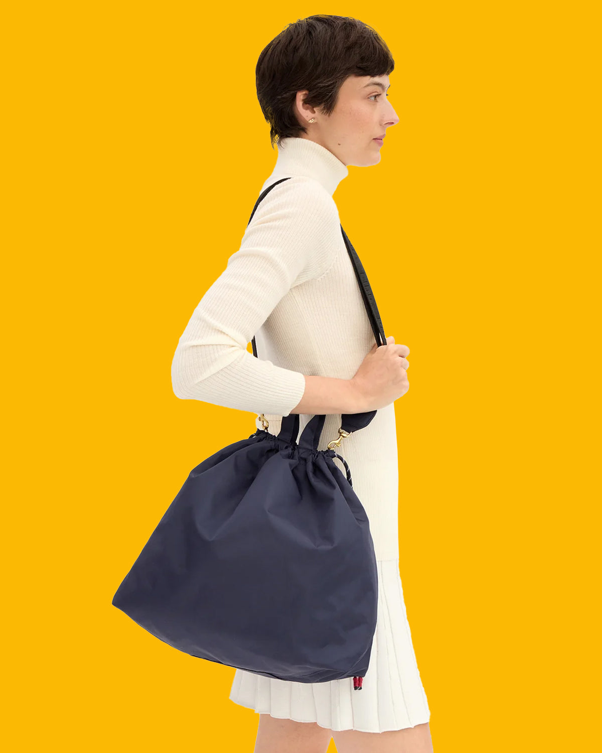 Model wearing a monochromatic cream outfit and carrying the Navy Sac Tout with the adjustable strap over her shoulder. 
