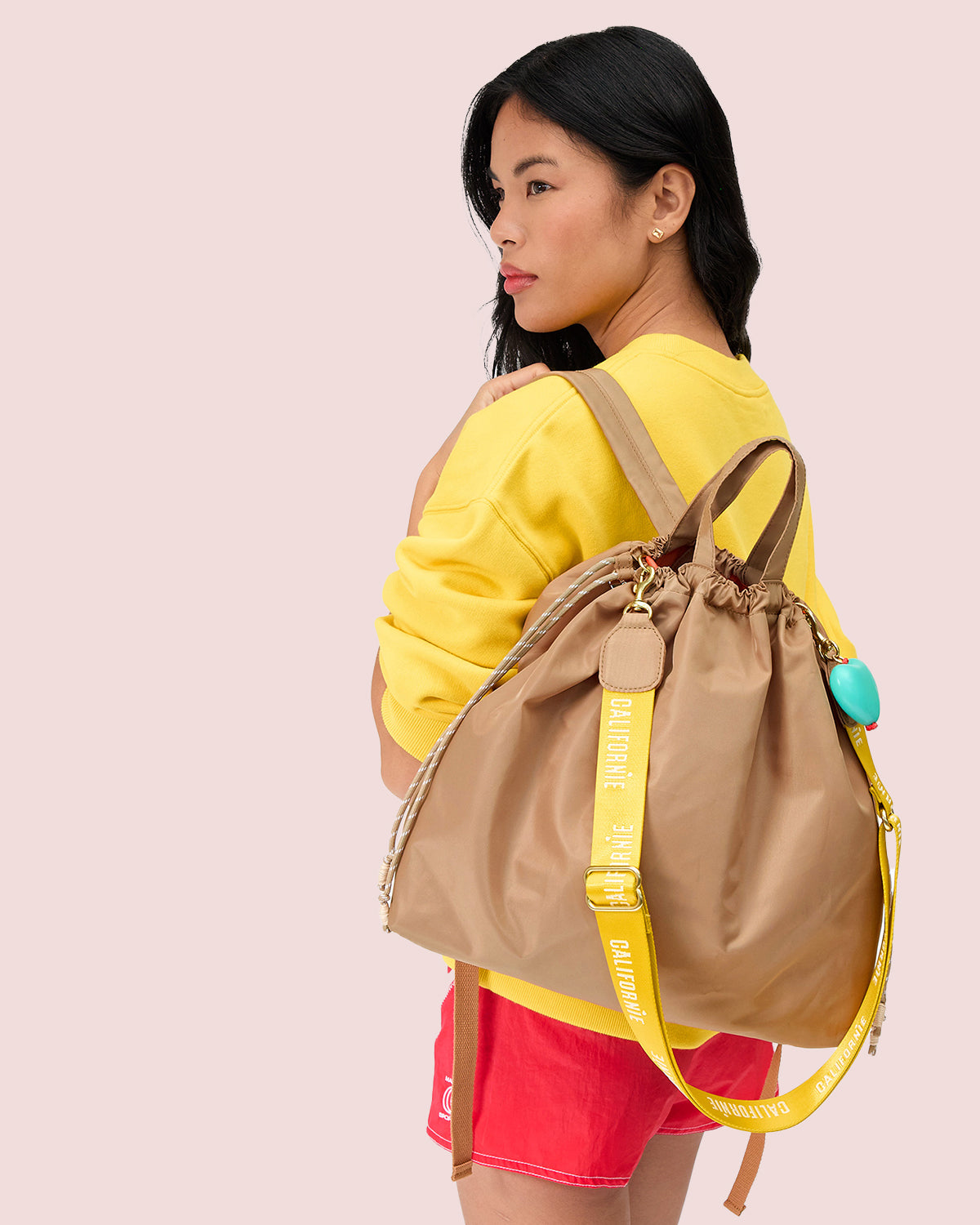 Model carrying the Latte Sac Tout Backpack with Turquoise Grande Heart Fob attached to it.
