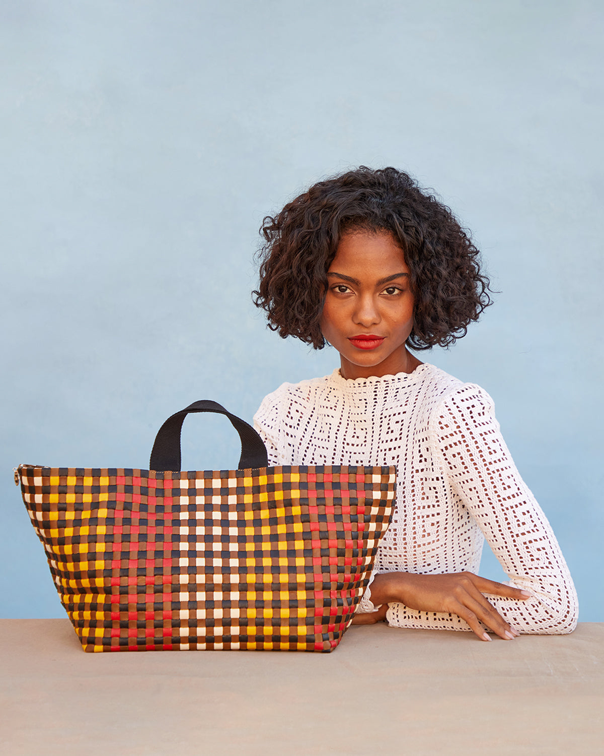 Model sitting next to the Harlequin Woven Checker Bateau Tote. 