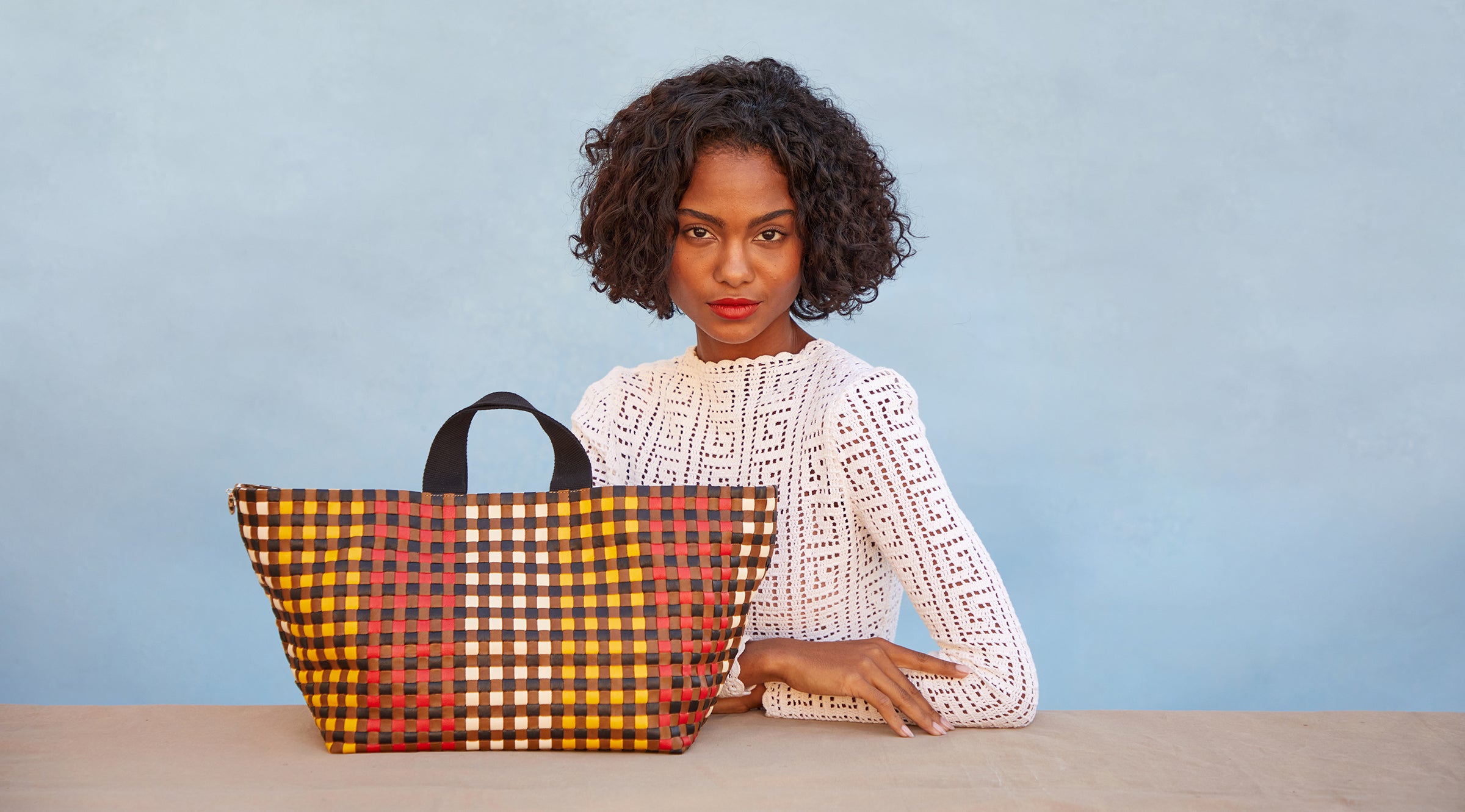 Model sitting next to the Harlequin Woven Checker Bateau Tote. 