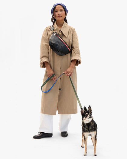 Model waring a khaki trench coat with the CV x The Dogist Bandana on her head, Grande Fanny with Adjustable Strap across her chest. Model is also holding onto a dog using the Clare V. x The Dogist leash. 