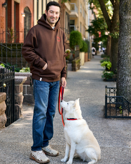 Elias Weiss Friedman wearing the Clare V. x The Dogist Beau Hoodie and standing next to a beautiful white dog that's wearing the Clare V. x The Dogist leash and collar. 
