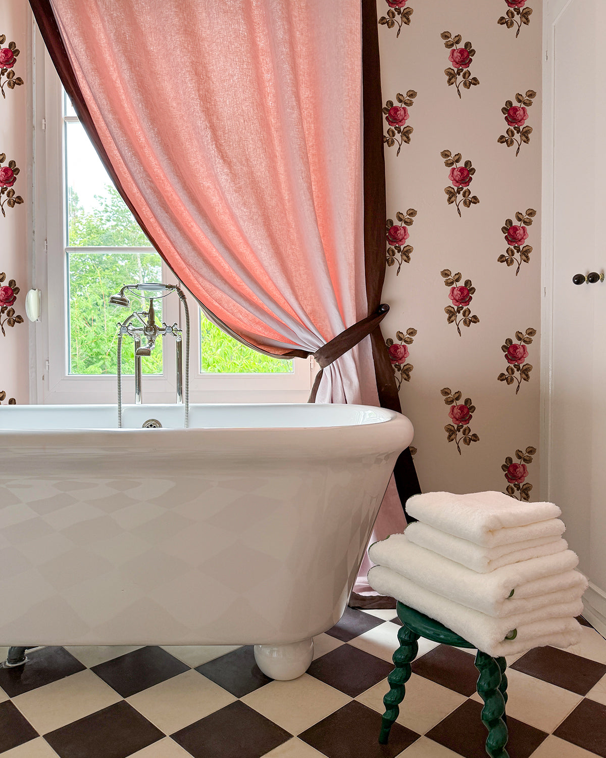 Bathroom with checkered tile, pink curtain, and Clare V. x Wallshoppe floral wallpaper.