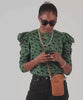 Mecca carrying the Tan Poche Sportif as a crossbody bag and opening it to take her cellphone out of the bag to use.