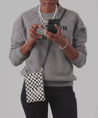 Mecca wearing the Black and White Checkered Poche across her body. She's also using a card to make a payment on her phone and then putting her phone inside of the Poche and Credit Card inside of the small exterior pocket.  