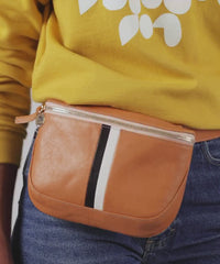 Mecca wearing the Natural with Black and White Stripes Fanny Pack around her waist and taking out her sunglasses from inside to put on her face. 