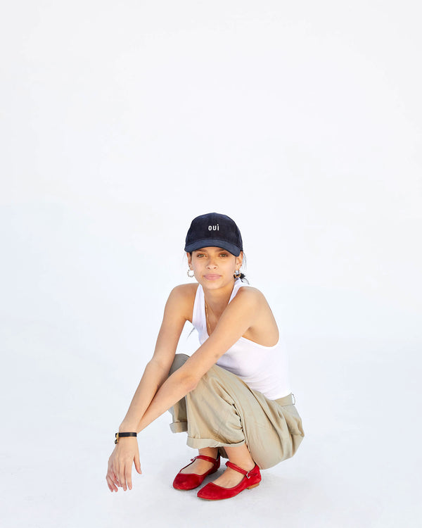 Aurelia wearing the Navy Corduroy Baseball Hat. she's crouching down and wearing red flats