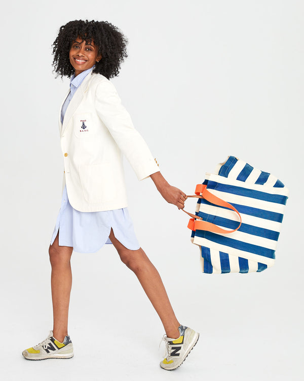 Mecca taking a step wearing a blue shirt-dress and a white blazer. she's holding the Azul & Shell Beach Tote  in her left hand