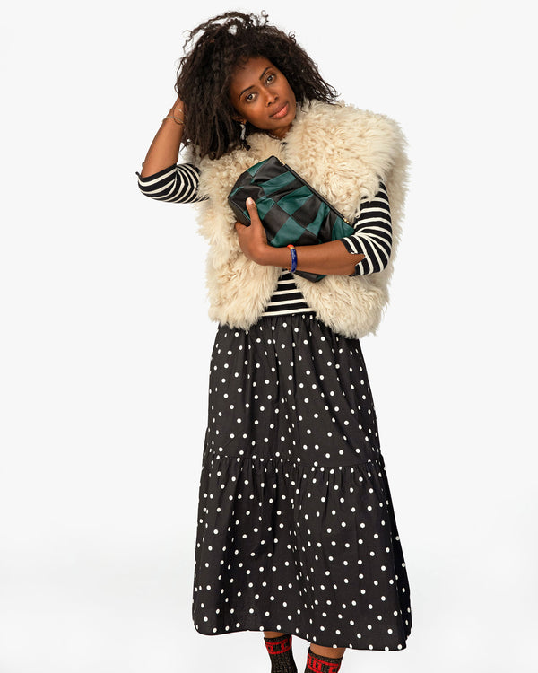 mecca wearing a fuzzy sherpa vest, a polka dot skirt holding the Black & Deep Sea Belle as a clutch