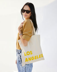 Aurelia is wearing acid wash jeans and a tan sweater with the Natural Oui Canvas Store Tote on her shoulder. 