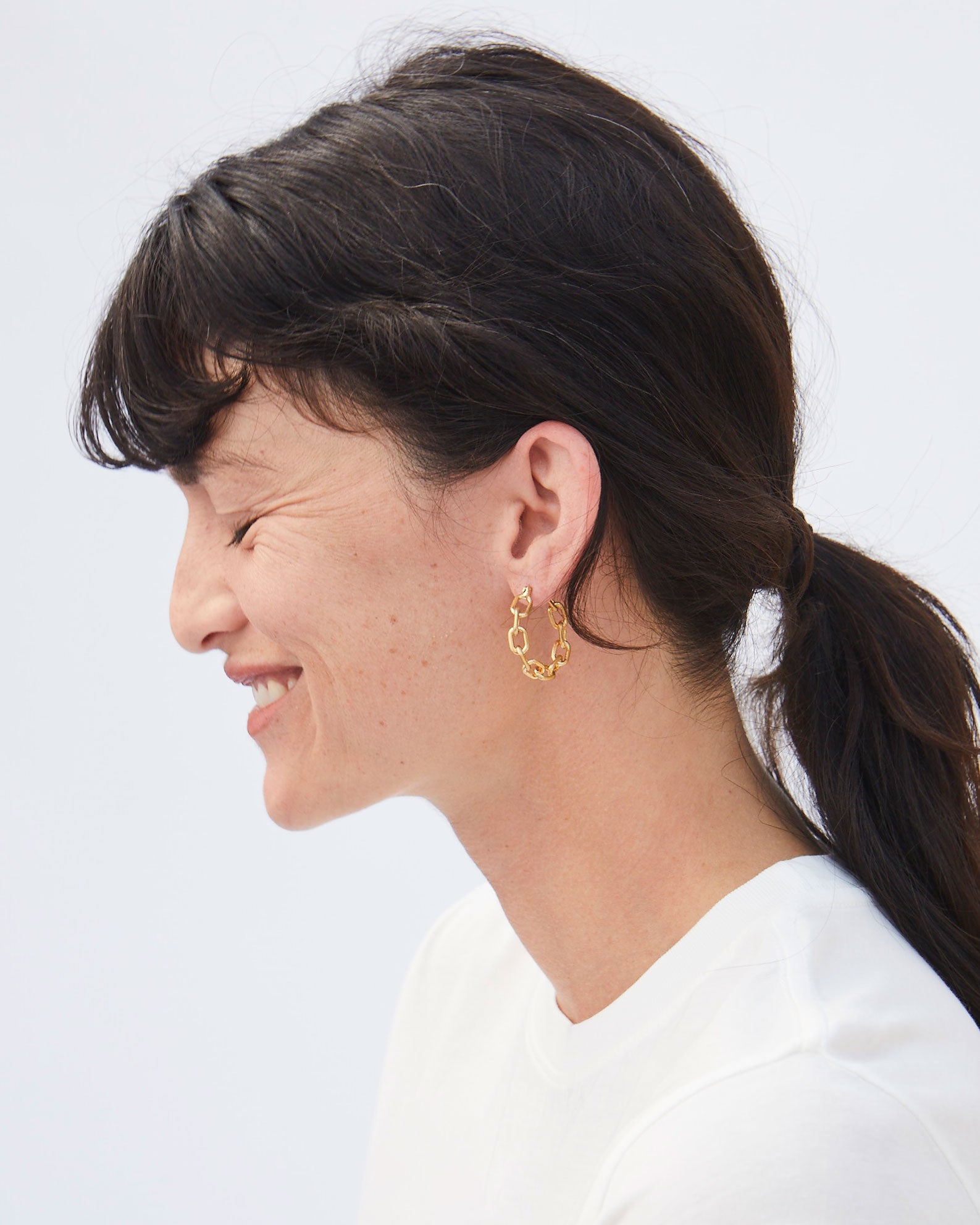 Side View of Danica Smiling ina  Wite T-Shirt and the Vintage Gold Chain Hoop Earrings with her Hair in a Ponytail