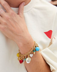 Vintage Gold Charm Chain Bracelet Shown with the Yellow Stone Bead Charm, Rattan Egg Charm, Fraise Charm, Cabochon Charm, Turquoise Petit Heart Charm, Gold Dipped Shell Charm, Freshwater Pearl Mini Heart Charm, Mushroom Charm, Turquoise Stone Bead Charm, and the CV x EMC Heart Locket Charm Against Danica's White Sweatshirt
