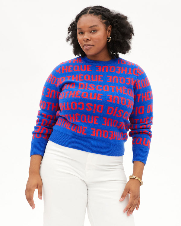 candace looking straight forward in the Cobalt & Poppy Discotheque Classic Sweater with white jeans with her hands relaxed at her side