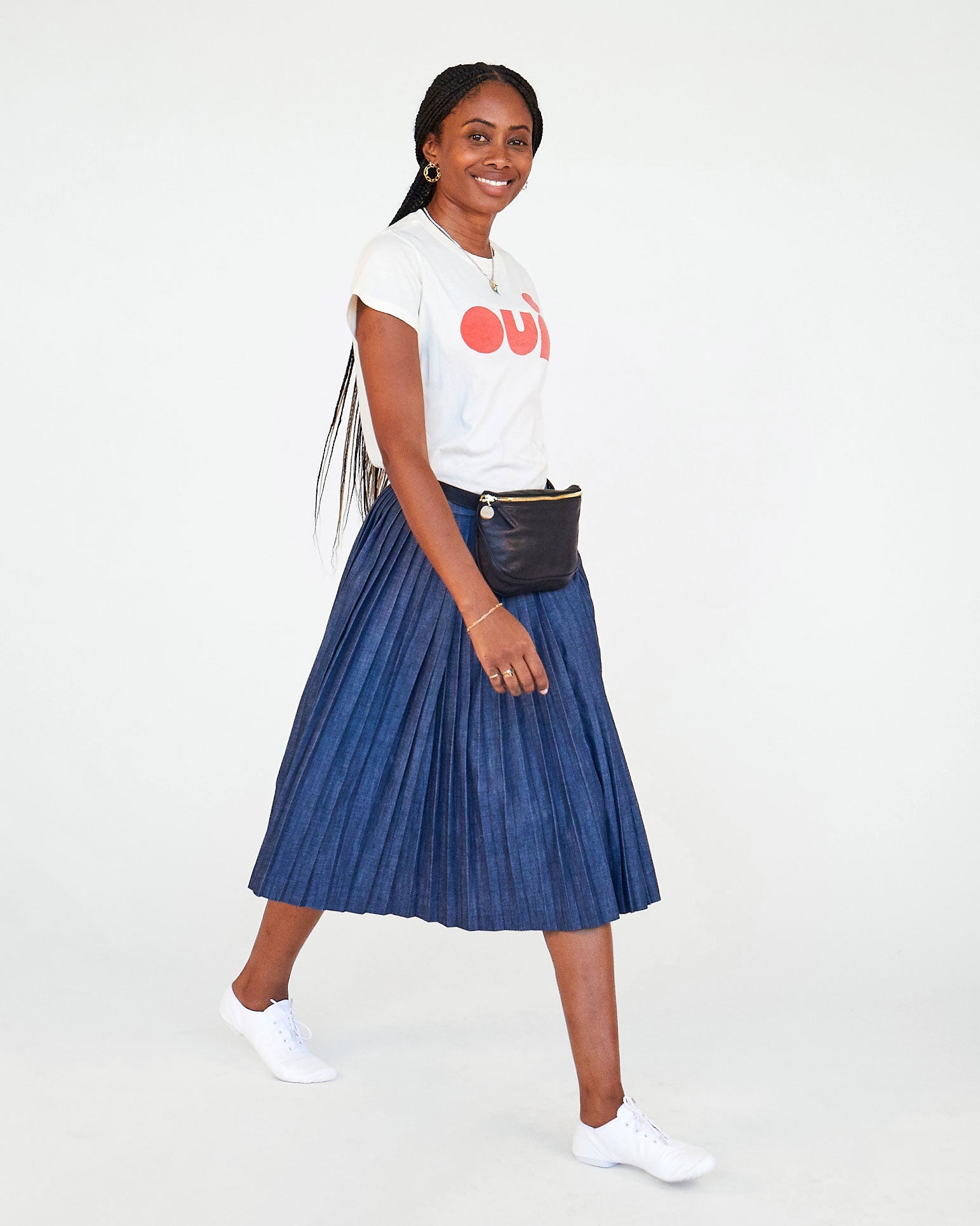 mecca in the Cream with Poppy Oui Classic Tee with a pleated navy skirt and the black fanny pack around her waist