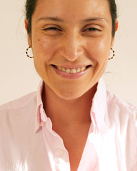 Andrea wearing the Black & Cream Enamel Stripe Hoop Earrings flashing a big smile at the camera. she's wearing a light pink button up shirt