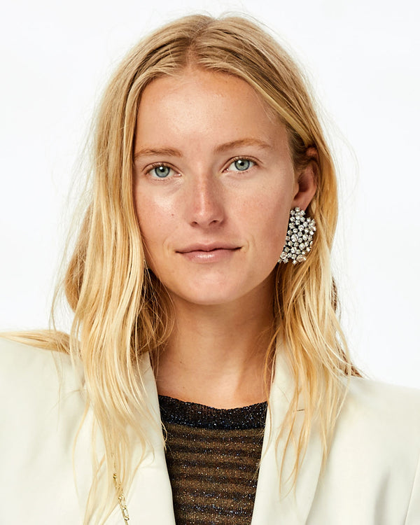 Natalie wearing a sparkly top and a white blazer with the Clear and Shiny Rhodium Finish Encrusted Statement Studs on, her hair tucked behind one ear