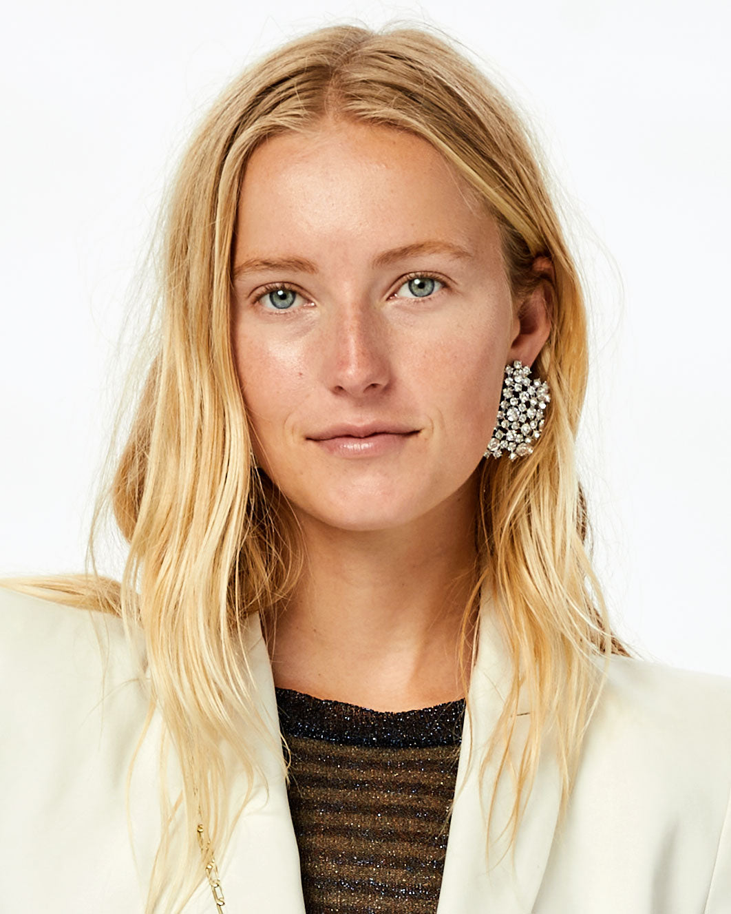 Natalie wearing a sparkly top and a white blazer with the Clear and Shiny Rhodium Finish Encrusted Statement Studs on, her hair tucked behind one ear