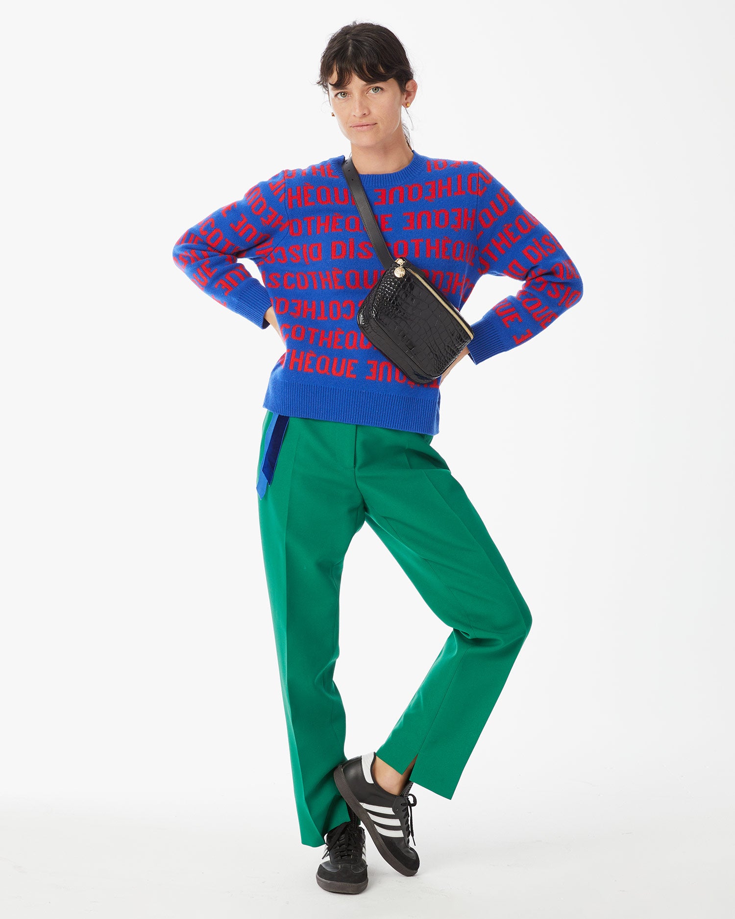 Danika wearing the Cobalt with Poppy Discotheque Classic Sweater with green pants and the Black Croco Fanny Pack across her chest. 