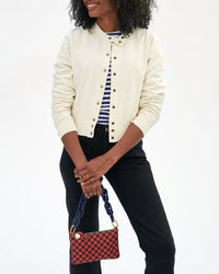 mecca in black jeans and a white jacket holding the Red and Navy Checker Wallet Clutch w/ Tabs  in front of her by the navy resin shortie strap