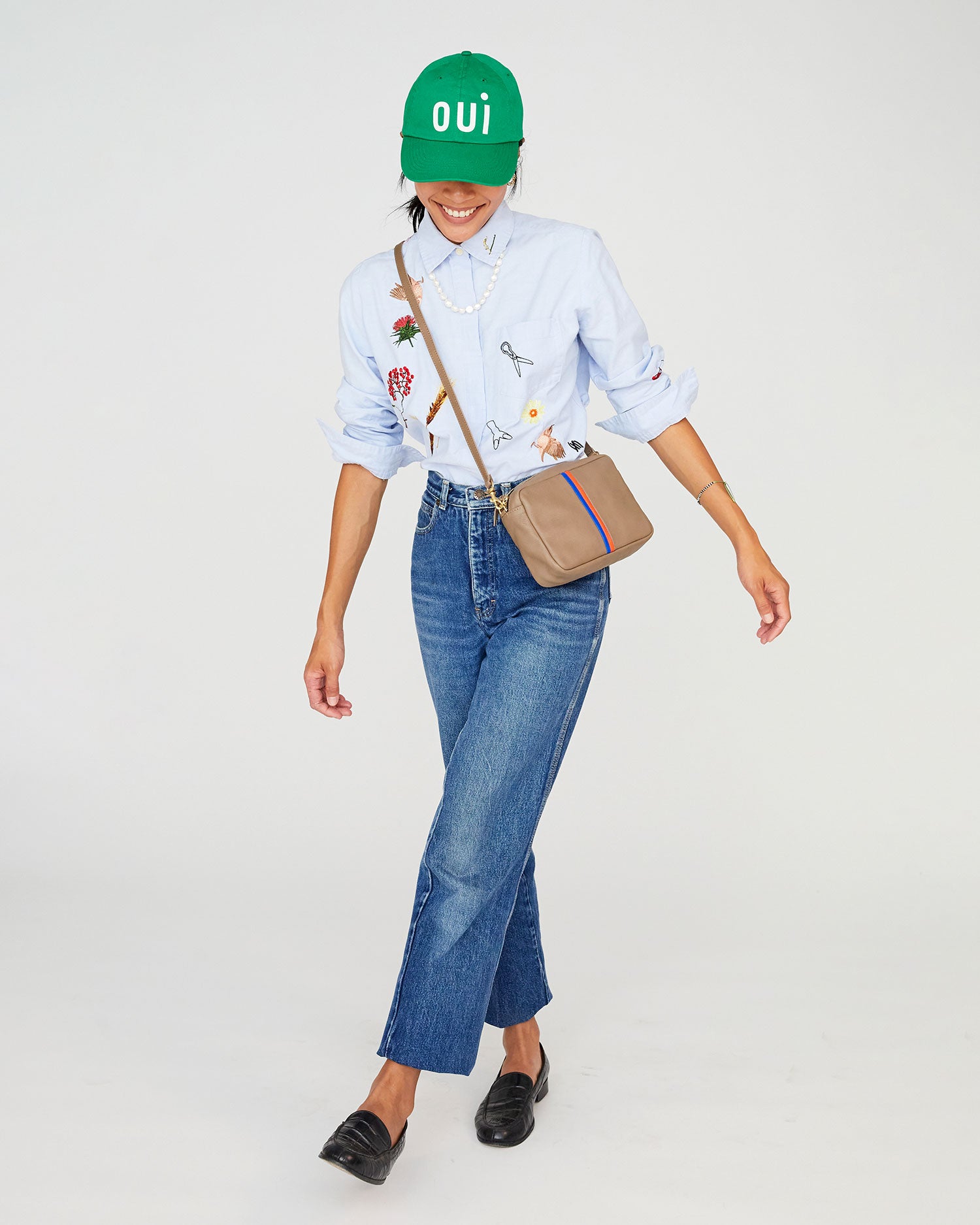 Sandra wearing the Green Oui Baseball Hat. she's wearing jeans and a button up shirt with the taupe mousse midi sac worn crossbody