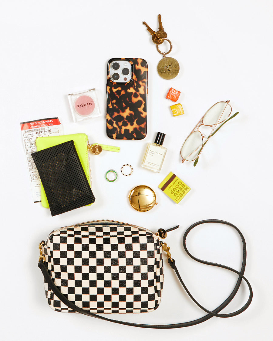 Black and white Checker Midi Sac shown with the items that fit inside. These items are a set of keys, a pair of glasses, a small perfume, a match book, a coin clutch, a blush, a card envelope, some rings and some starbursts.