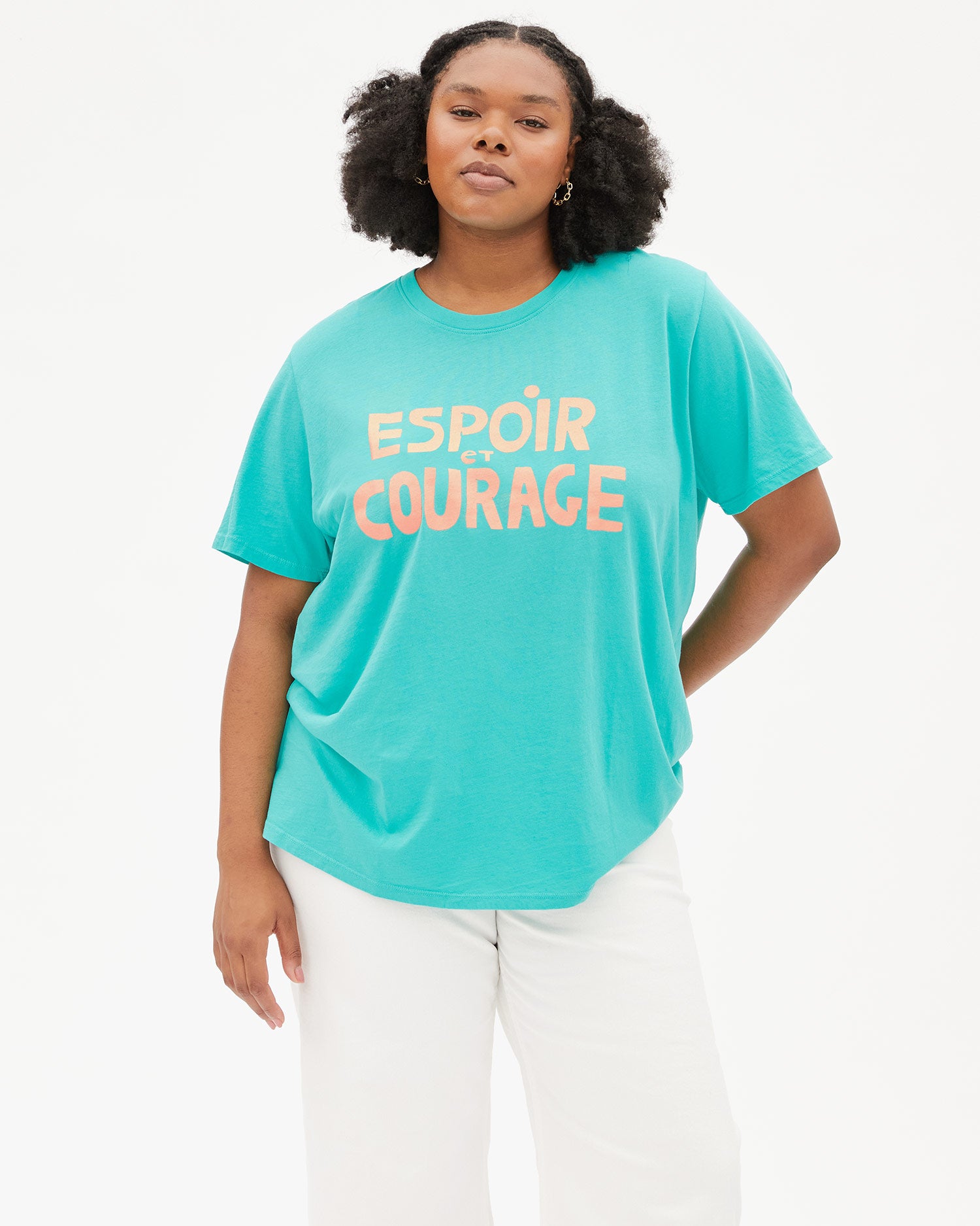 Candace wearing the Desert Turquoise Espoir et Courage Original Tee with white jeans with her left hand behind her back