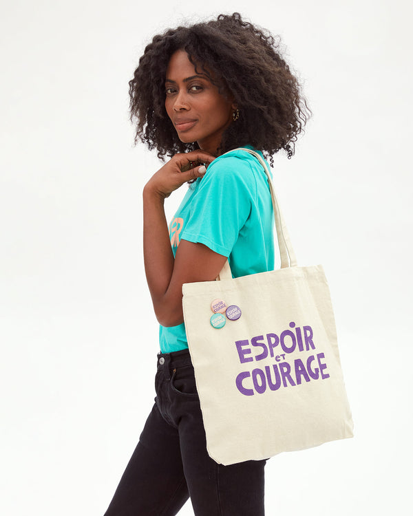 Mecca carrying the Clare V. x Gabrielle Giffords Canvas Tote w/ Pins printed with Espoir et Courage on her shoulder