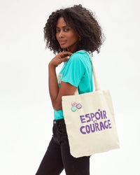Mecca carrying the Clare V. x Gabrielle Giffords Canvas Tote w/ Pins printed with Espoir et Courage on her shoulder
