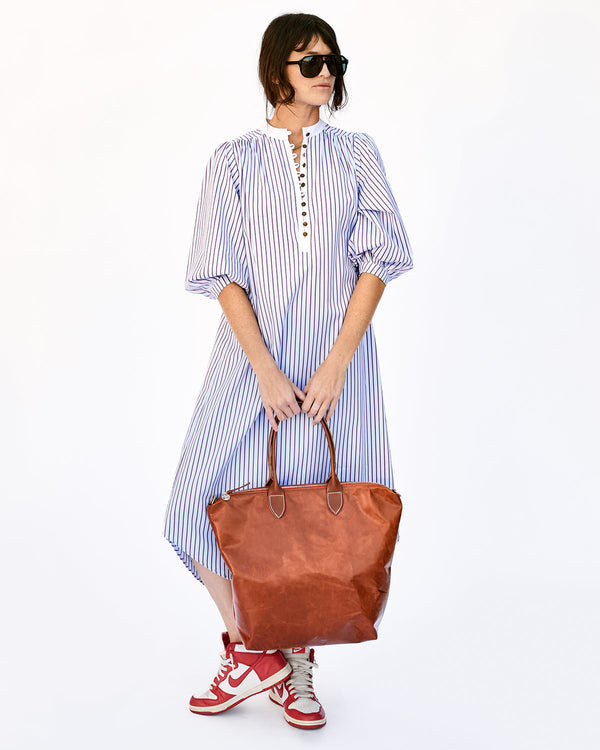 Danica in a Blue Striped Shift Dress and Jordans Holding the Camel Overnighter in Front of her With Both Hands