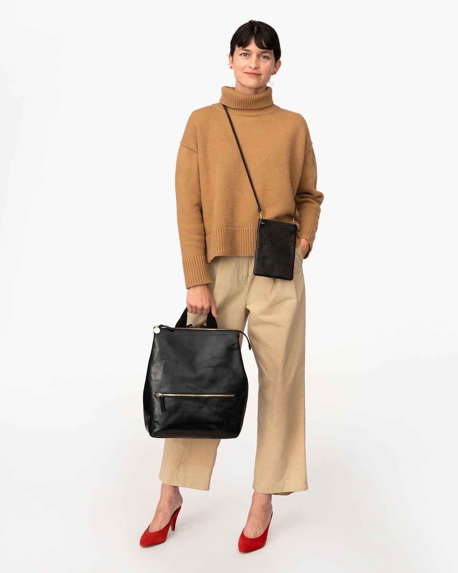 danica in an all tan outfit holding the Black Rustic Remi Backpack by its top handle with the black rustic poche worn crossbody