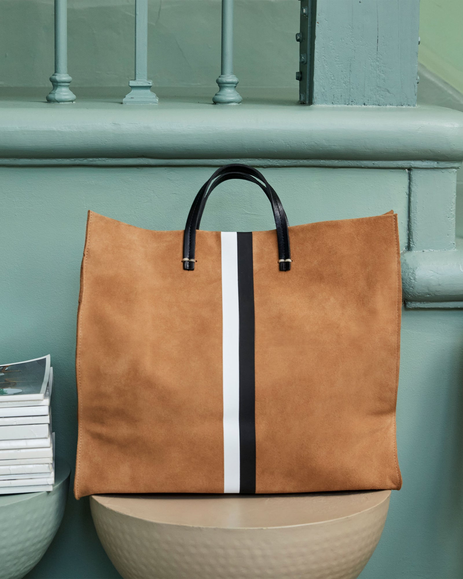 Simple Tote in Camel Suede w/Black & White Stripes sitting next to a green staircase. 